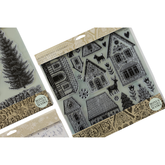 A package of clear silicone stamps with black printed Christmas-themed designs, including gingerbread houses, trees, snowflakes, and reindeer. A second stamp package with a Christmas tree design is partially visible on the left against a white background.
