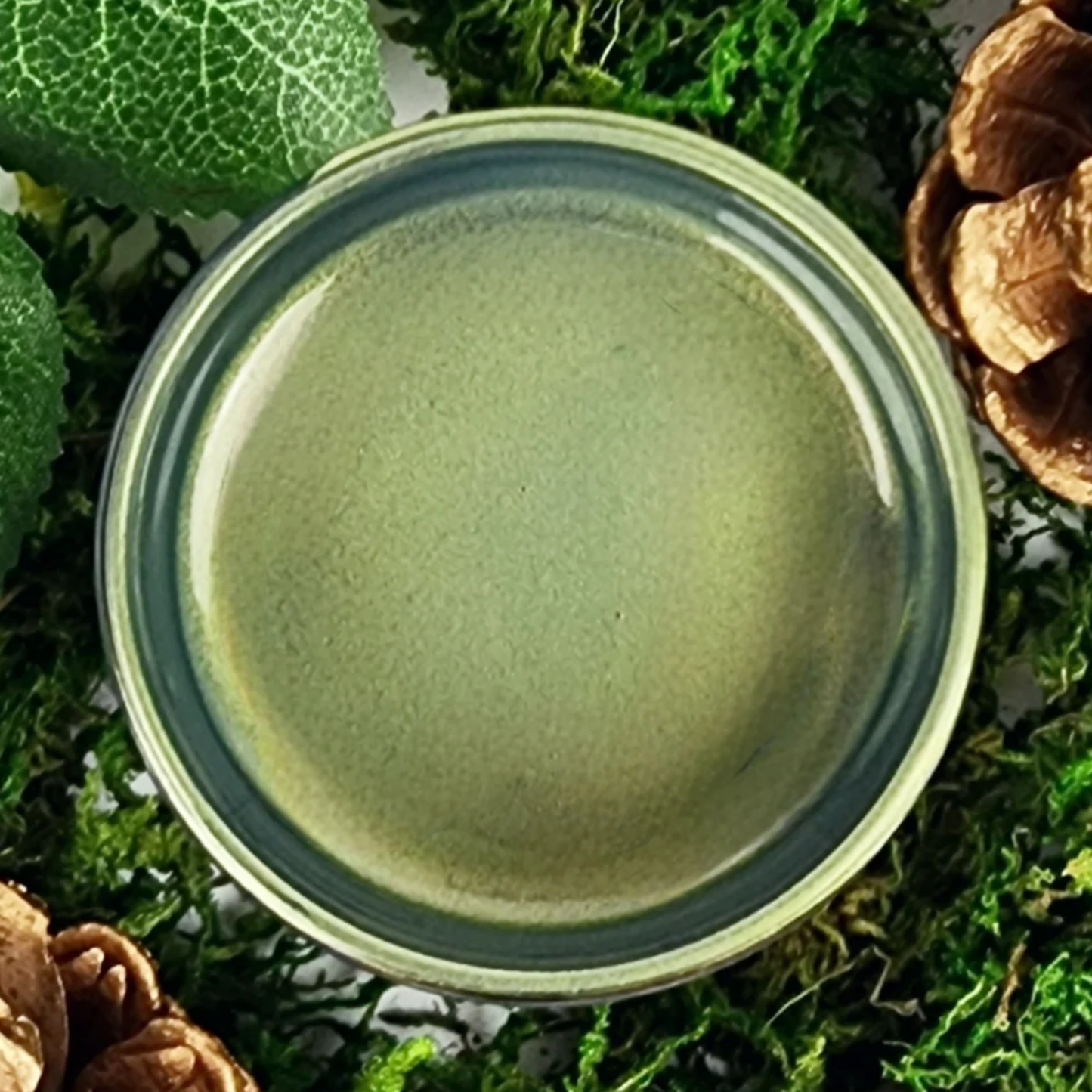 Jar of green metallic paint with textured surface on a natural background.