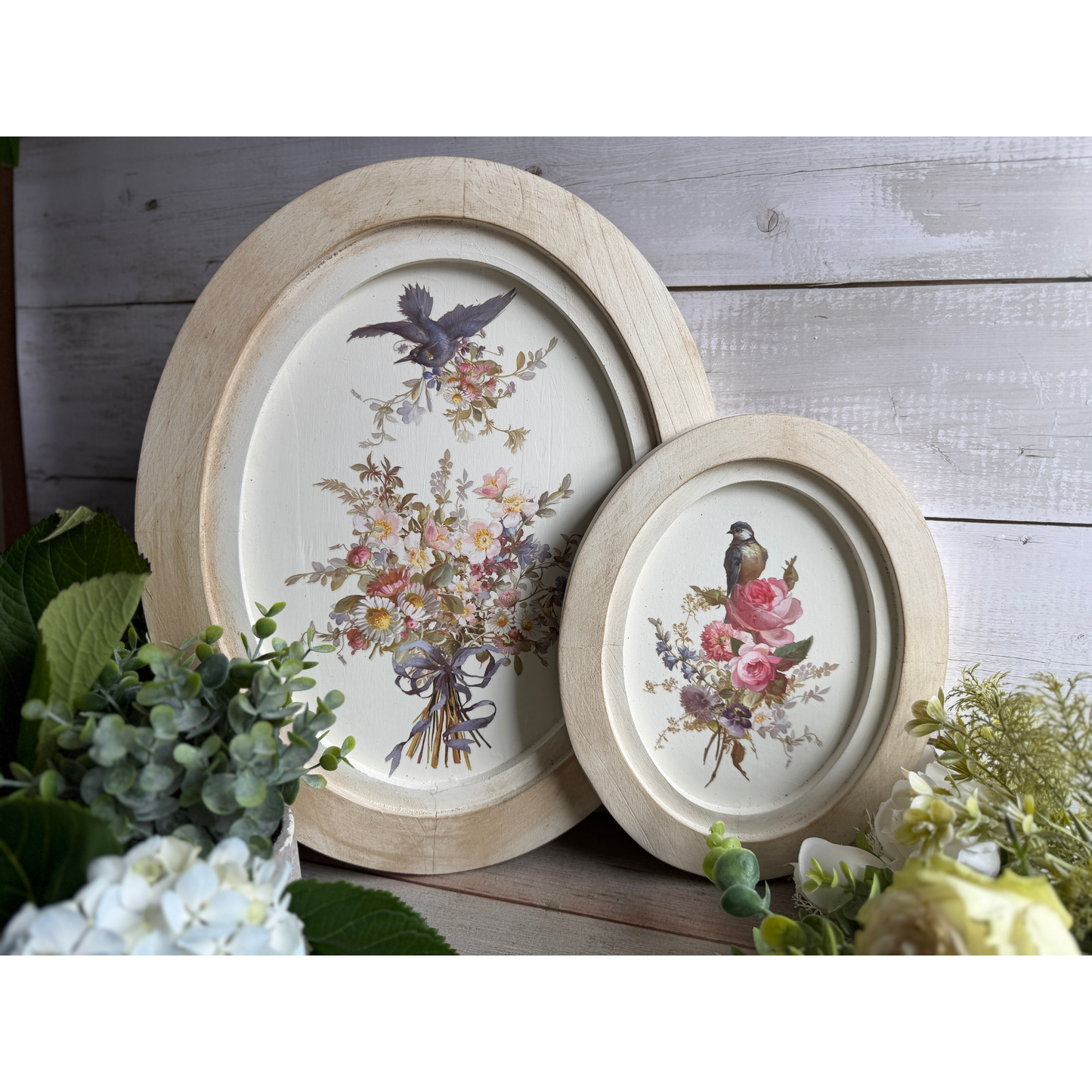 Two oval wooden frames with floral and bird designs on a wooden surface.
