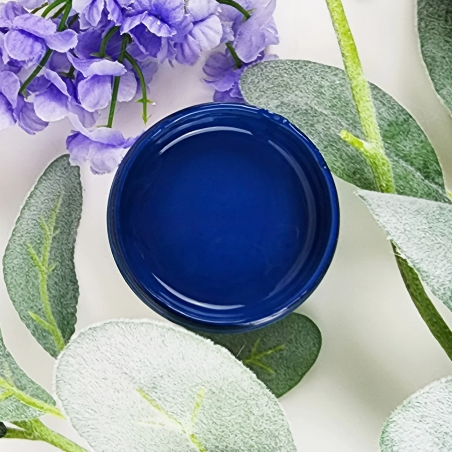 Image of open jar of deep blue paint with blue flowers and leaves on a white background.