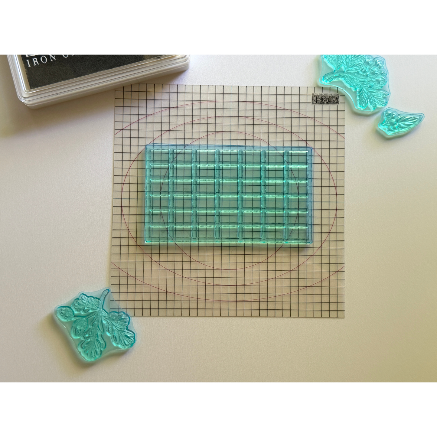 A clear stamp with a grid pattern, displayed on a gridded mini thin mount with leaf-shaped stamps and a stamp ink pad visible in the corner.