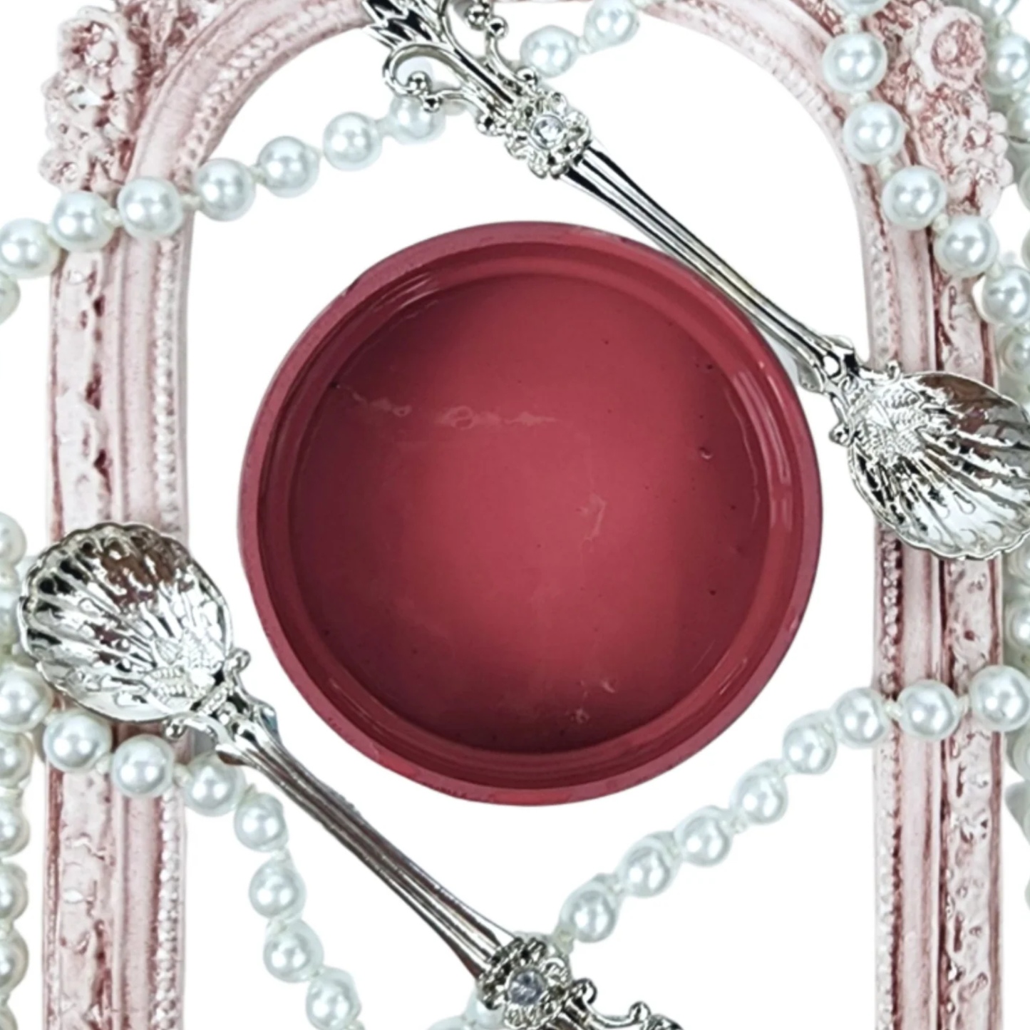 Image of open jar of burgundy colored paint with pearls, silver spoon and vintage frame on a white background.