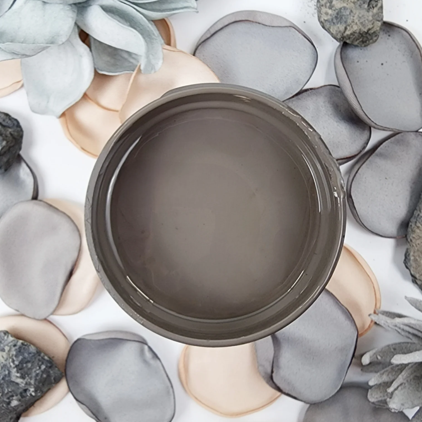 Image of open jar of taupe brown paint on a background of grey and peach flower petals.