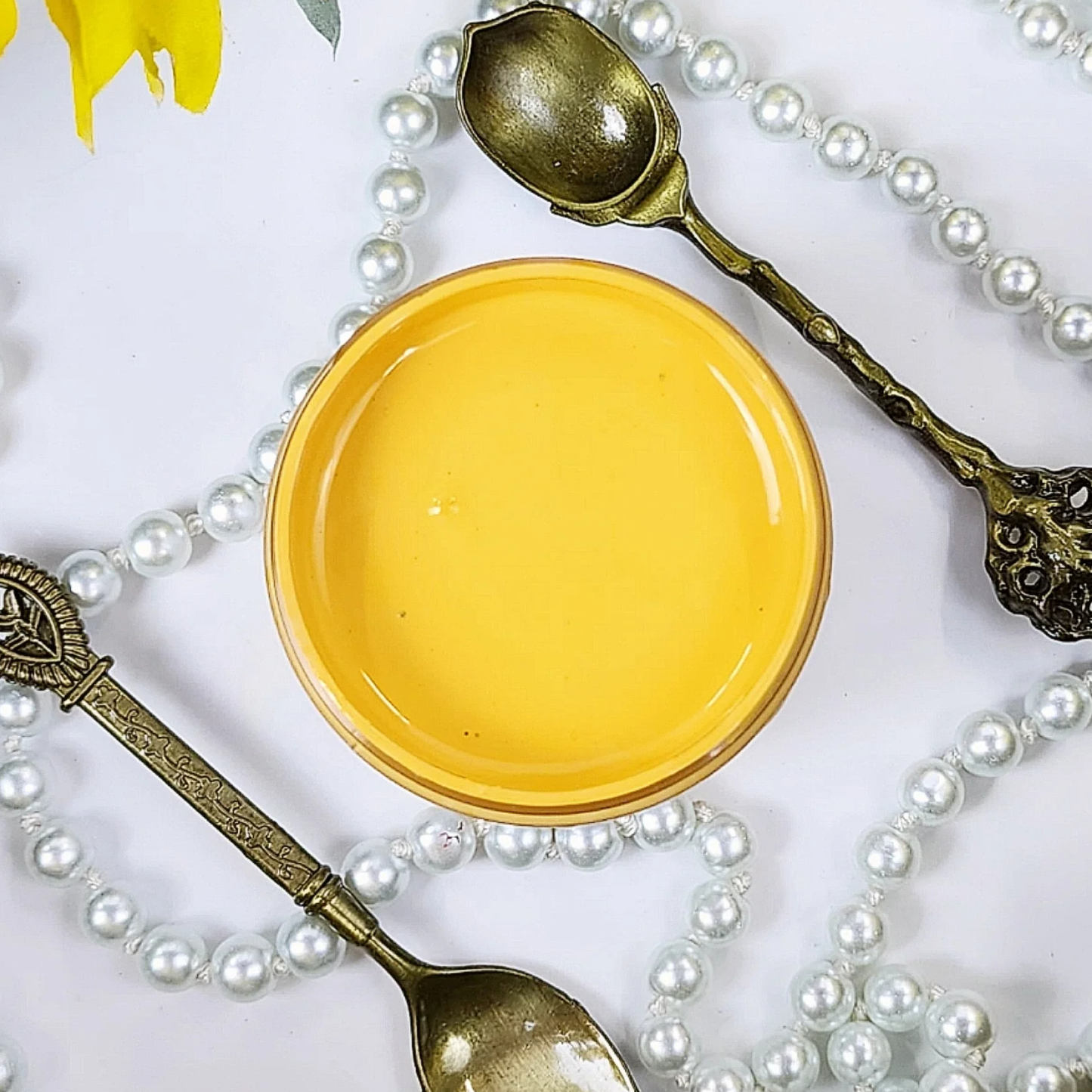 Image of an open jar of canary yellow paint with pears and silver spoons in the background.