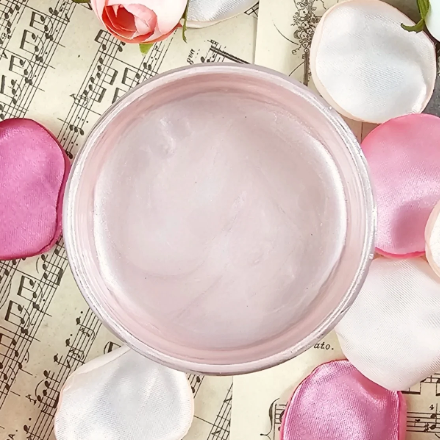 Jar of pink metallic paint surrounded by pink and white flowers on sheet music background