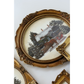 An ornate oval decorative mirror with a carved gold frame, reflecting a snowy winter landscape with trees and a horse-drawn carriage.
