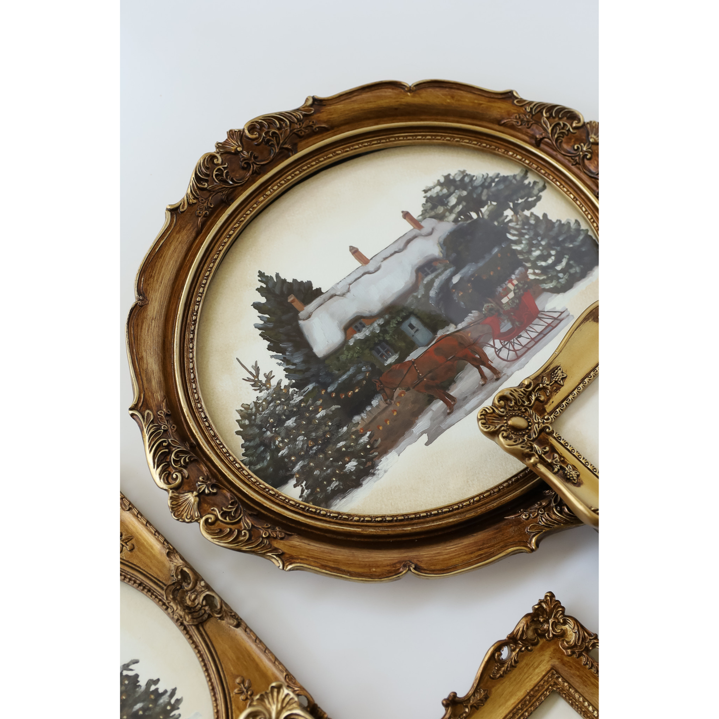 An ornate oval decorative mirror with a carved gold frame, reflecting a snowy winter landscape with trees and a horse-drawn carriage.