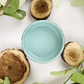 Image of open jar of light blue/green paint with wood chips and leaves on a white background.