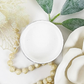 Image of open jar of bright white paint with white rose, leaves and beige beads on a white background.