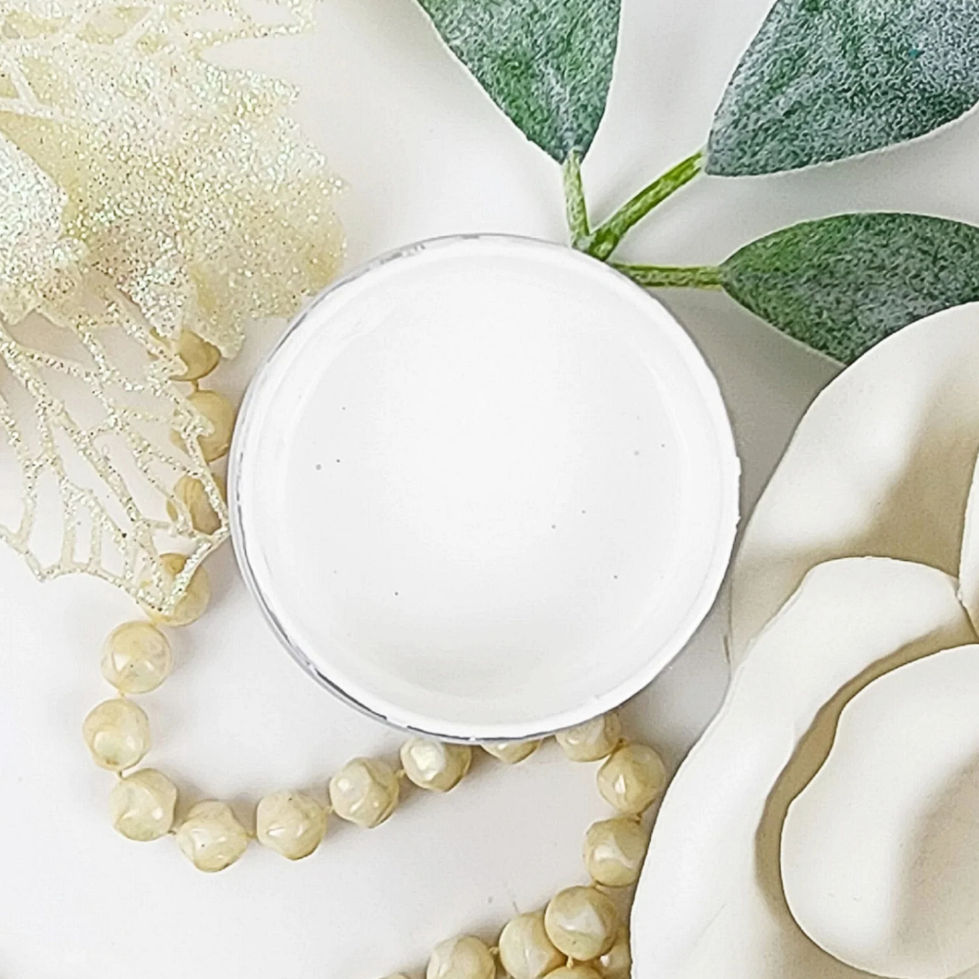 Image of open jar of bright white paint with white rose, leaves and beige beads on a white background.