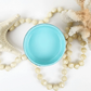 Image of open jar of light turquoise paint with coral, starfish and beige beads on a white background.