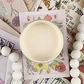 Image of open jar of creamy beige colored paint on colorful postcards in background.