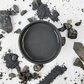 Image of open jar of dark charcoal grey paint with crushed pieces of coal on a white background.