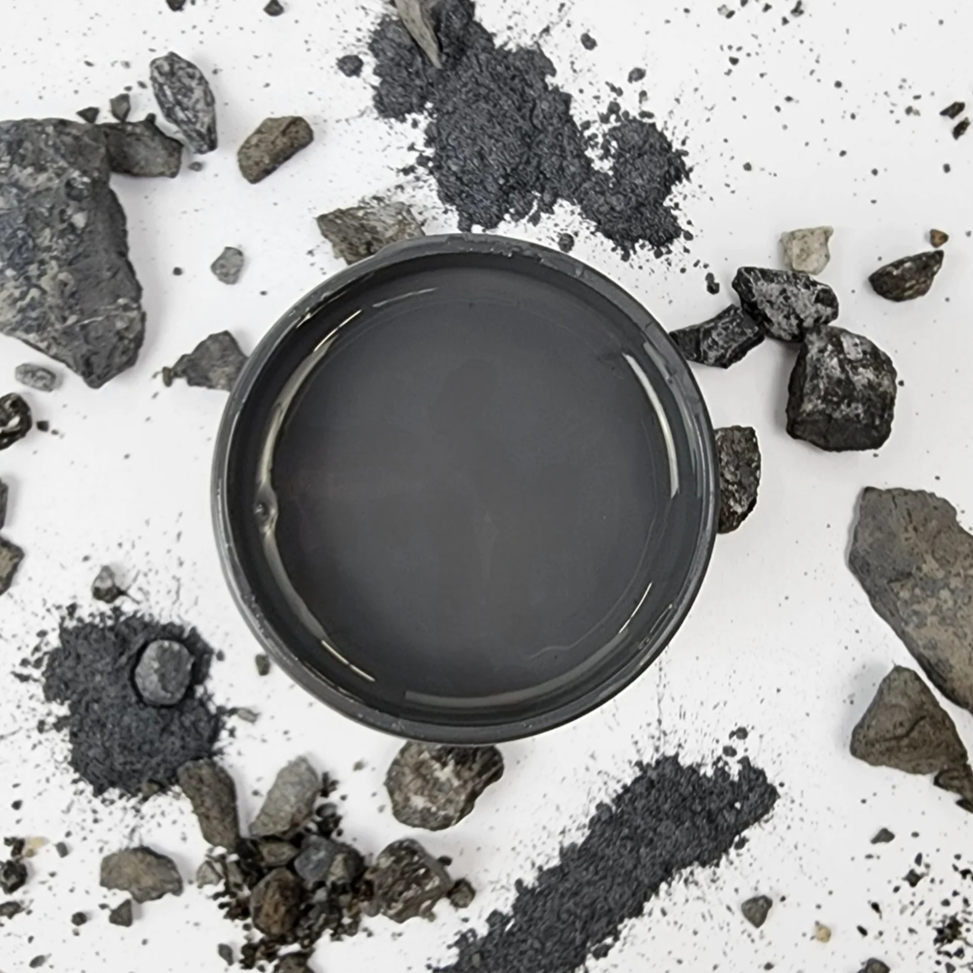 Image of open jar of dark charcoal grey paint with crushed pieces of coal on a white background.