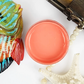 Image of open jar of deep coral colored paint with colorful ceramic fish, starfish and beads on a white background.
