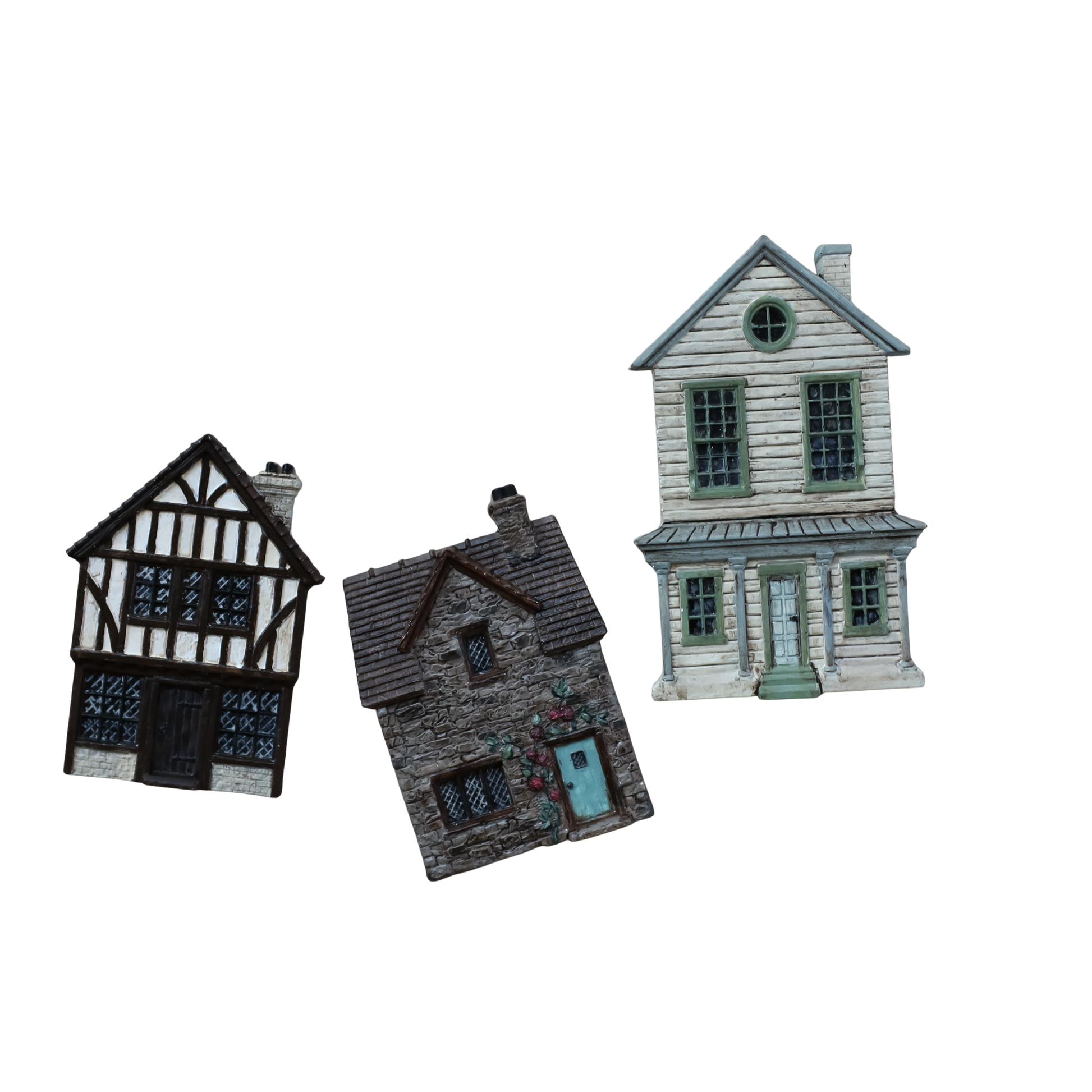 Three miniature painted decorative houses shown on a plain white background: a black-and-white timber-framed house, a gray stone house with a turquoise door, and a pale gray house with green trim., all from the Charlbury Lane and Old Colchester Road IOD Moulds.