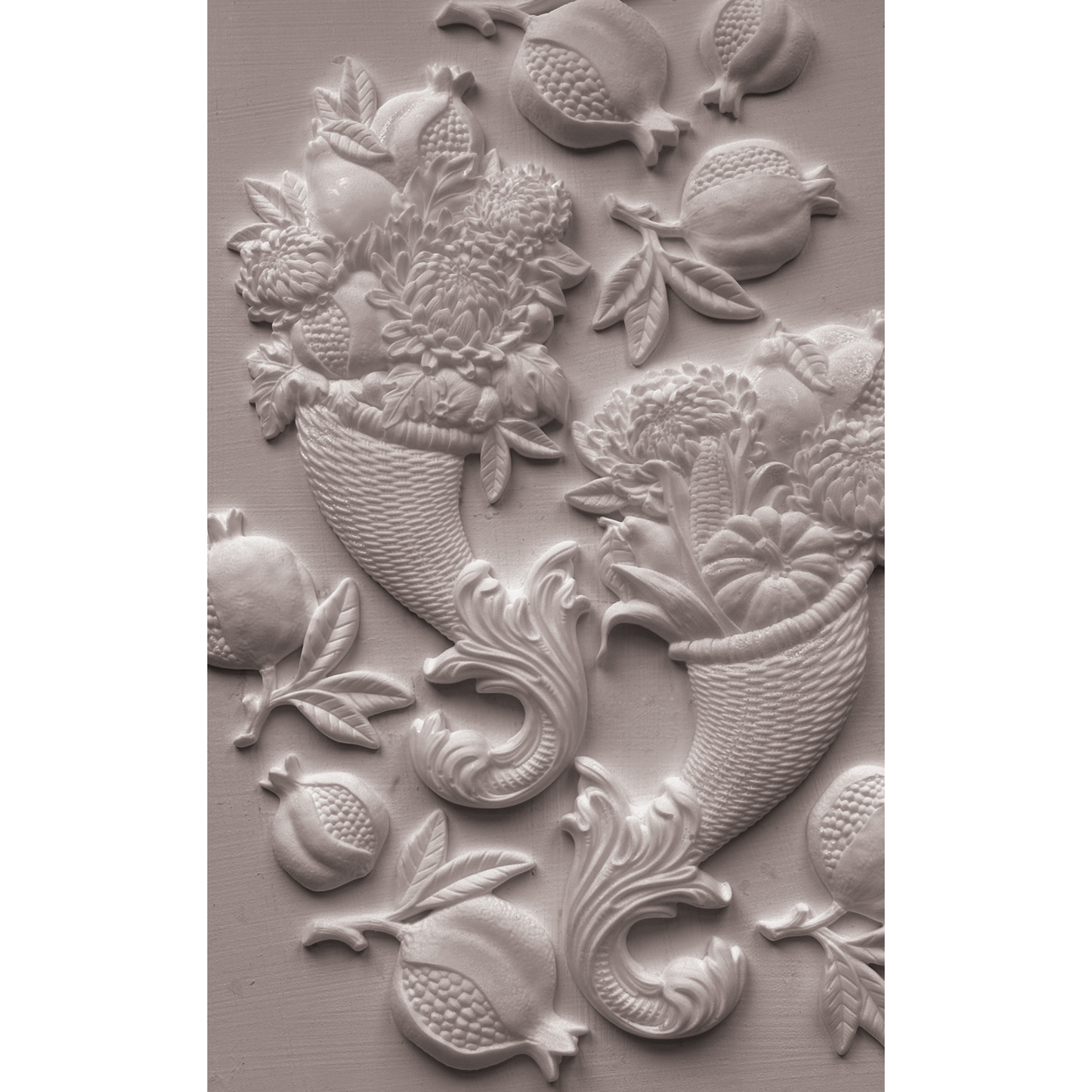 A close-up of a white castng featuring a classic fruit and floral cornucopia motif, including pomegranates, cherries, and bouquets, set against a matching textured background.