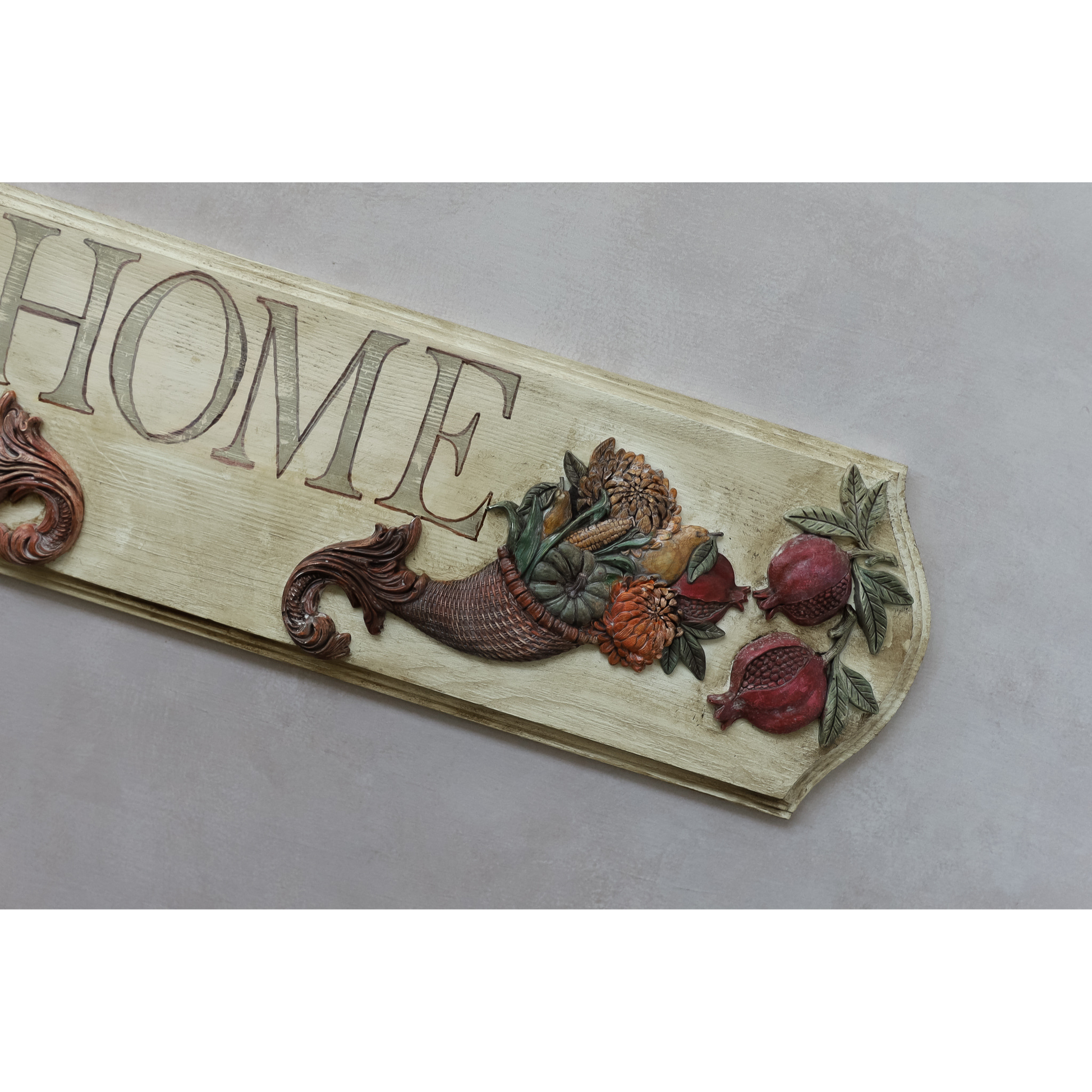 A rustic decorative wooden sign with the word 'HOME' in painted letters, decorated with a cornucopia and pomegranate motifs on a light beige background.