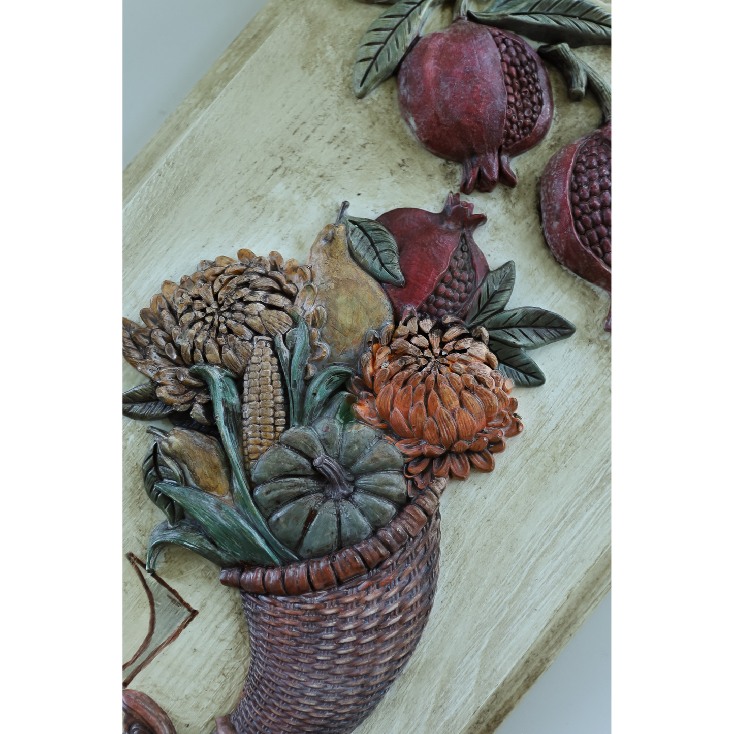 A close-up of a decorative wooden wall piece featuring a relief of a harvest cornucopia with a pomegranate, pear, pumpkin, and leaves on a light wood background.