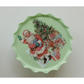 A scalloped-edge ceramic plate or dish in pale mint green, featuring a vintage-style IOD transfer image of Santa Claus sitting next to a decorated Christmas tree and wrapped gifts.
