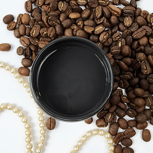 Image of open jar of deep brown colored paint with tarnished pearls and coffee beans on a white background.
