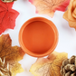 Image of open jar of bright orange paint with autumn colored leaves, flowers and pine cones on a white background.