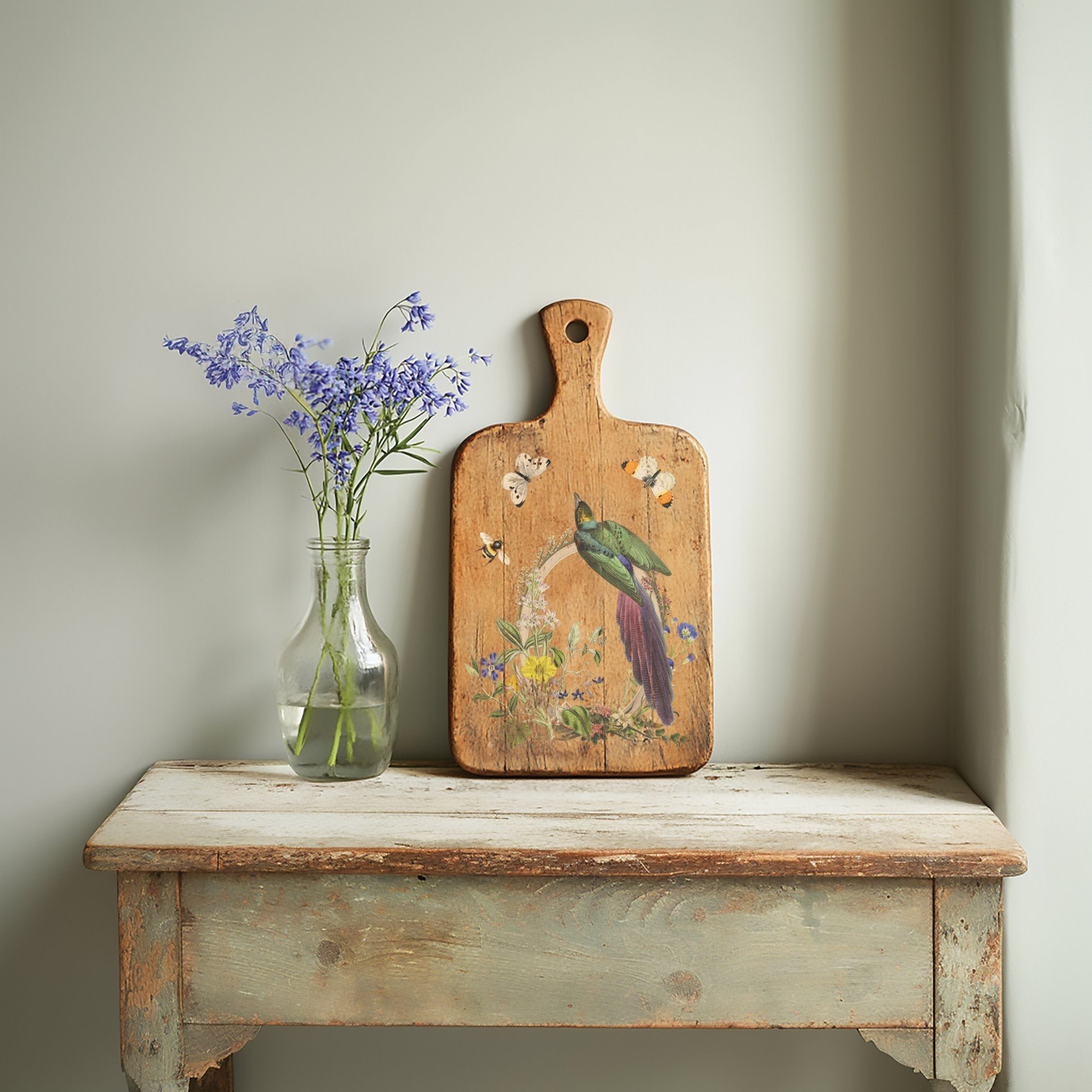 Vintage wooden bench with a vase of flowers and a decorative cutting board against a light wall.