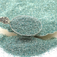 Silver spoon filled with pale turquoise glitter.