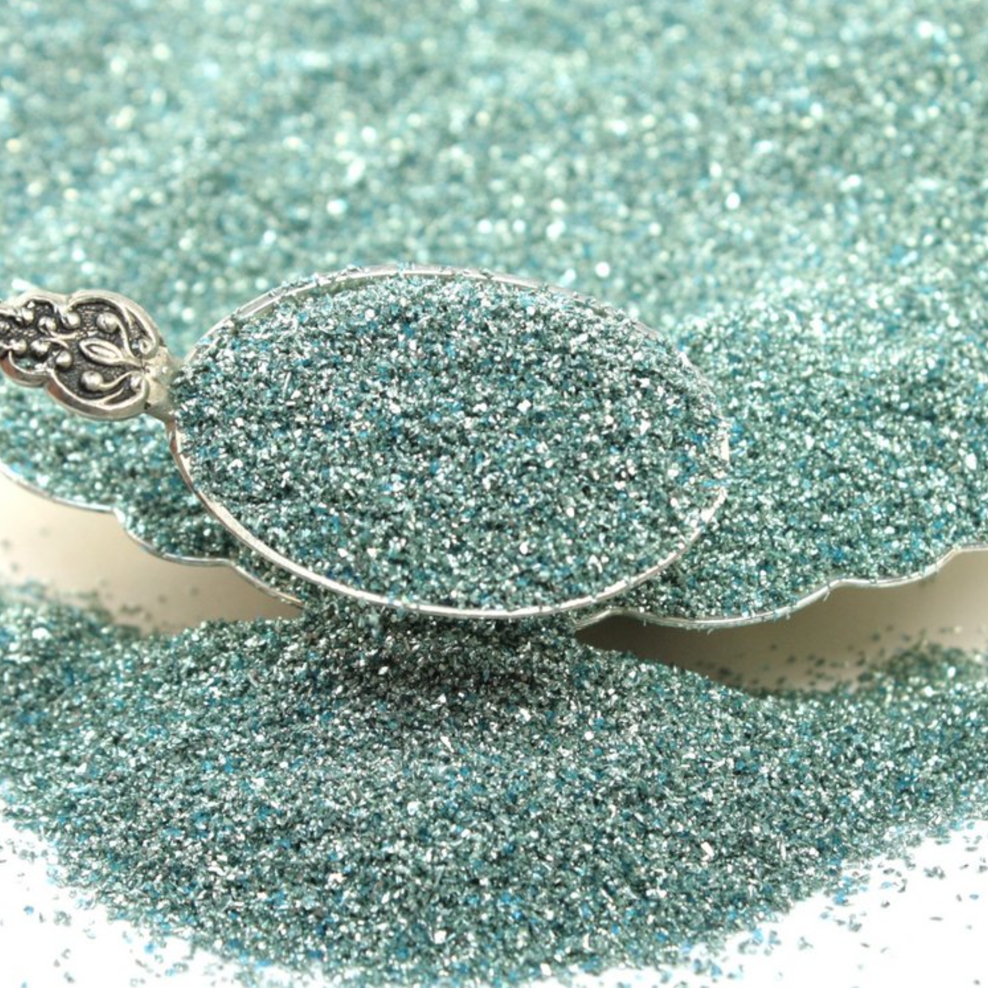 Silver spoon filled with pale turquoise glitter.