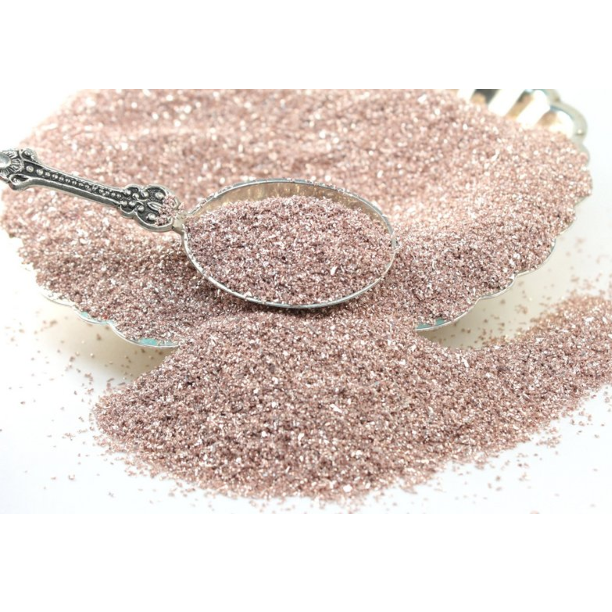 Silver spoon on a pile of pale pink glitter with a white background