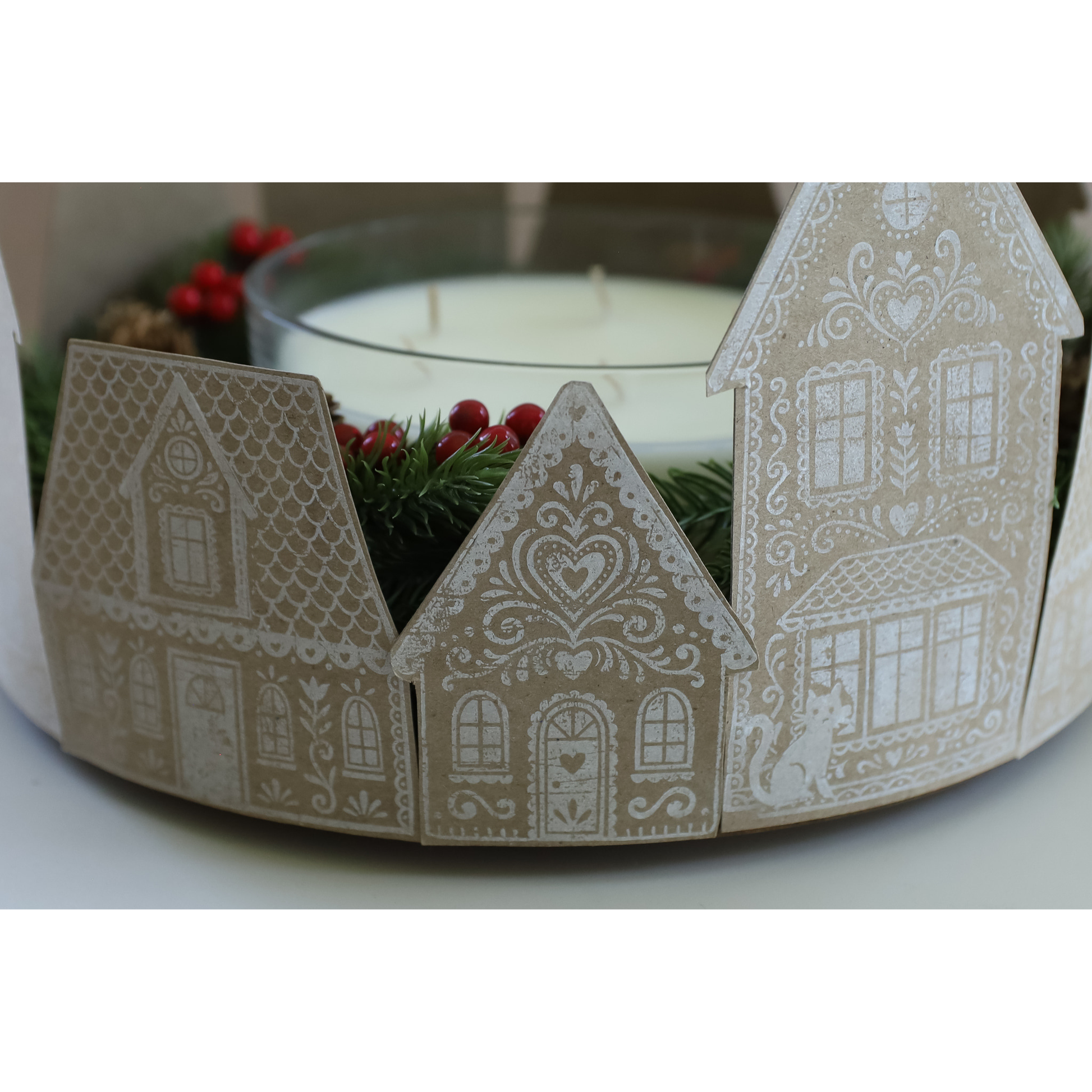 House-shaped ornaments with white printed patterns on kraft paper, shown around a white candle with red berries in the background.