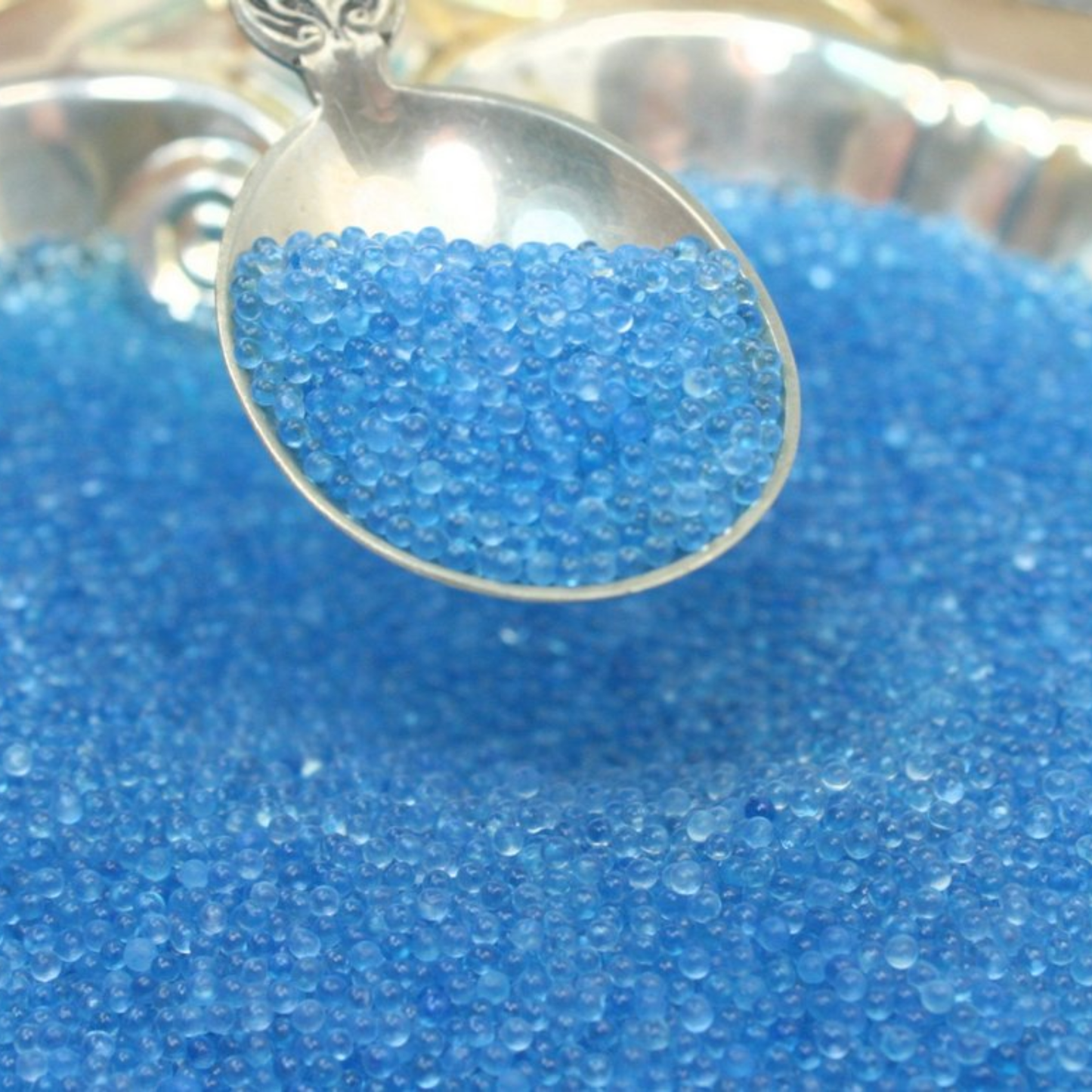 Silver spoon filled with blue translucent beads on a bed of blue beads.