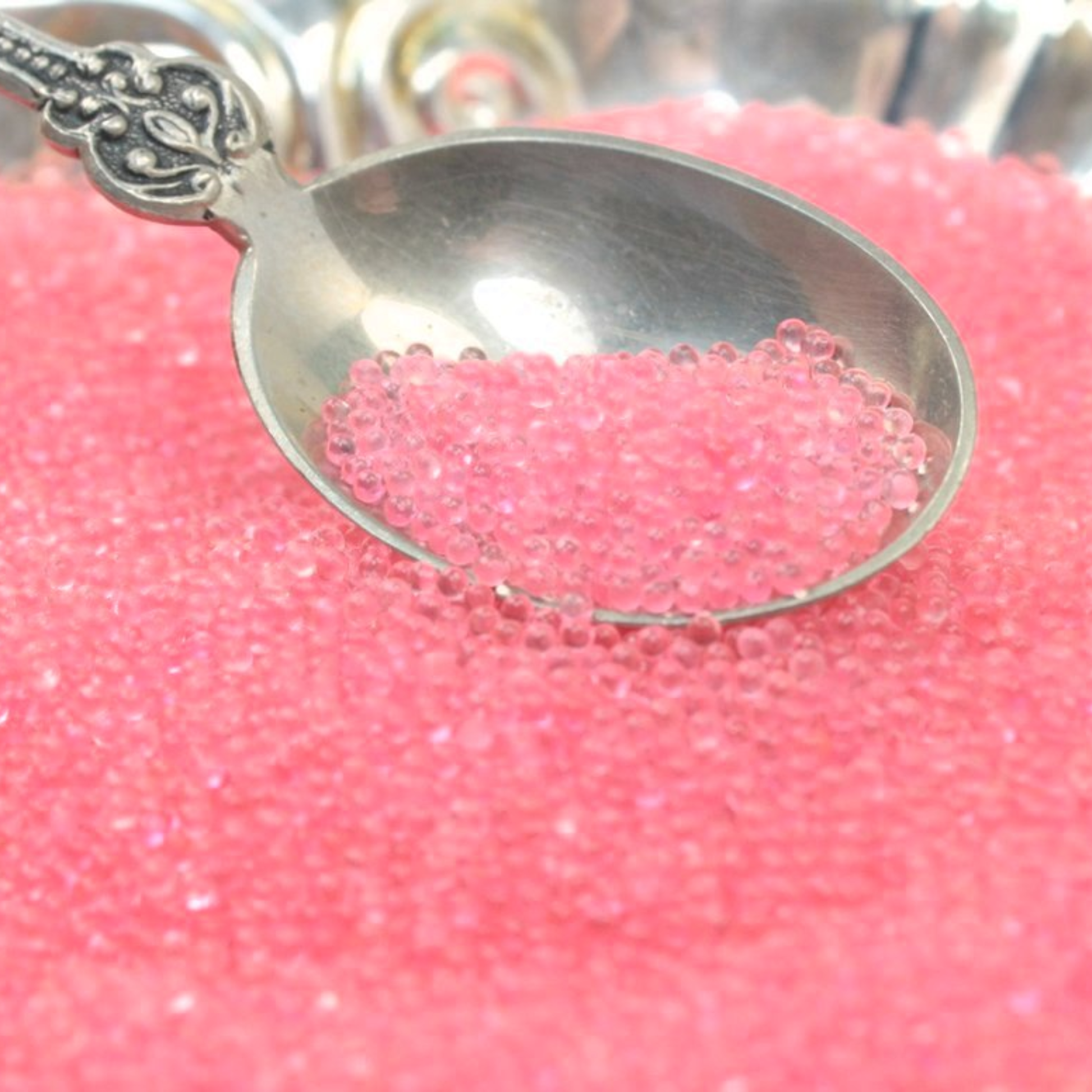 Silver spoon with translucent pink glass beads on a pink background