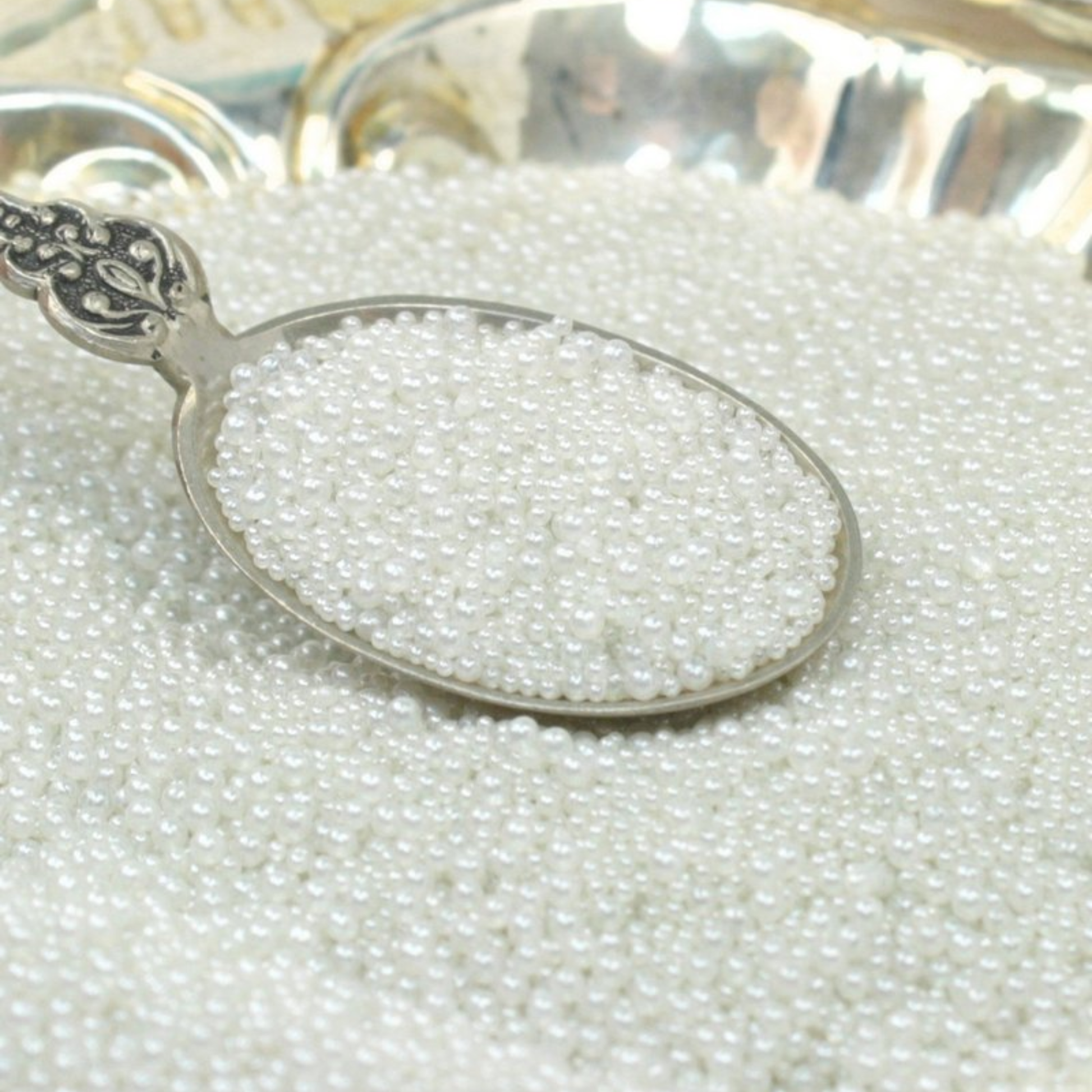 Silver spoon filled with small white pearls on a bed of pearls.