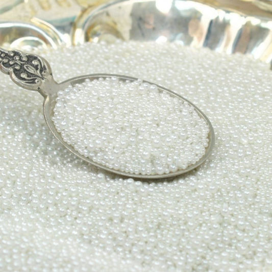 Silver spoon filled with small white pearls on a bed of pearls.