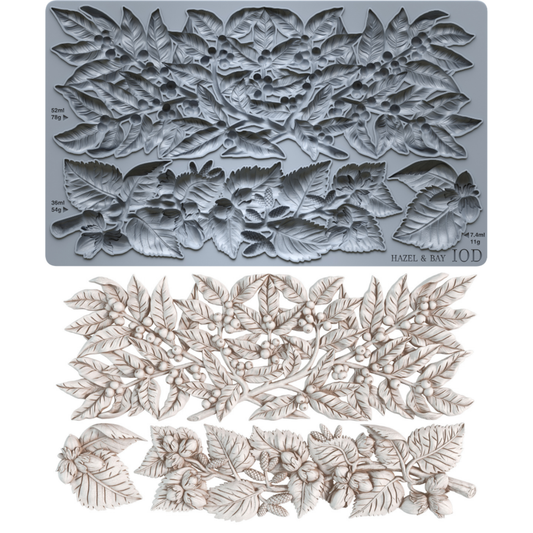 A gray silicone mold with embossed holly and bay leaf patterns, shown above a set of matching light beige carved leaf and berry ornaments. The mold has printed dimensions and the text 'HAZEL & BAY' and '10D'.