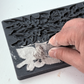 A close-up of a hand pressing clay into a silicone mould with floral and leaf designs