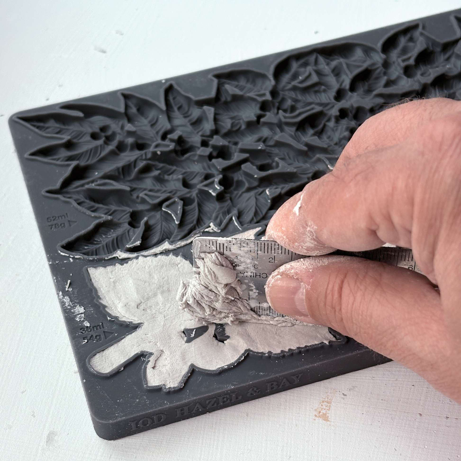 A close-up of a hand pressing clay into a silicone mould with floral and leaf designs