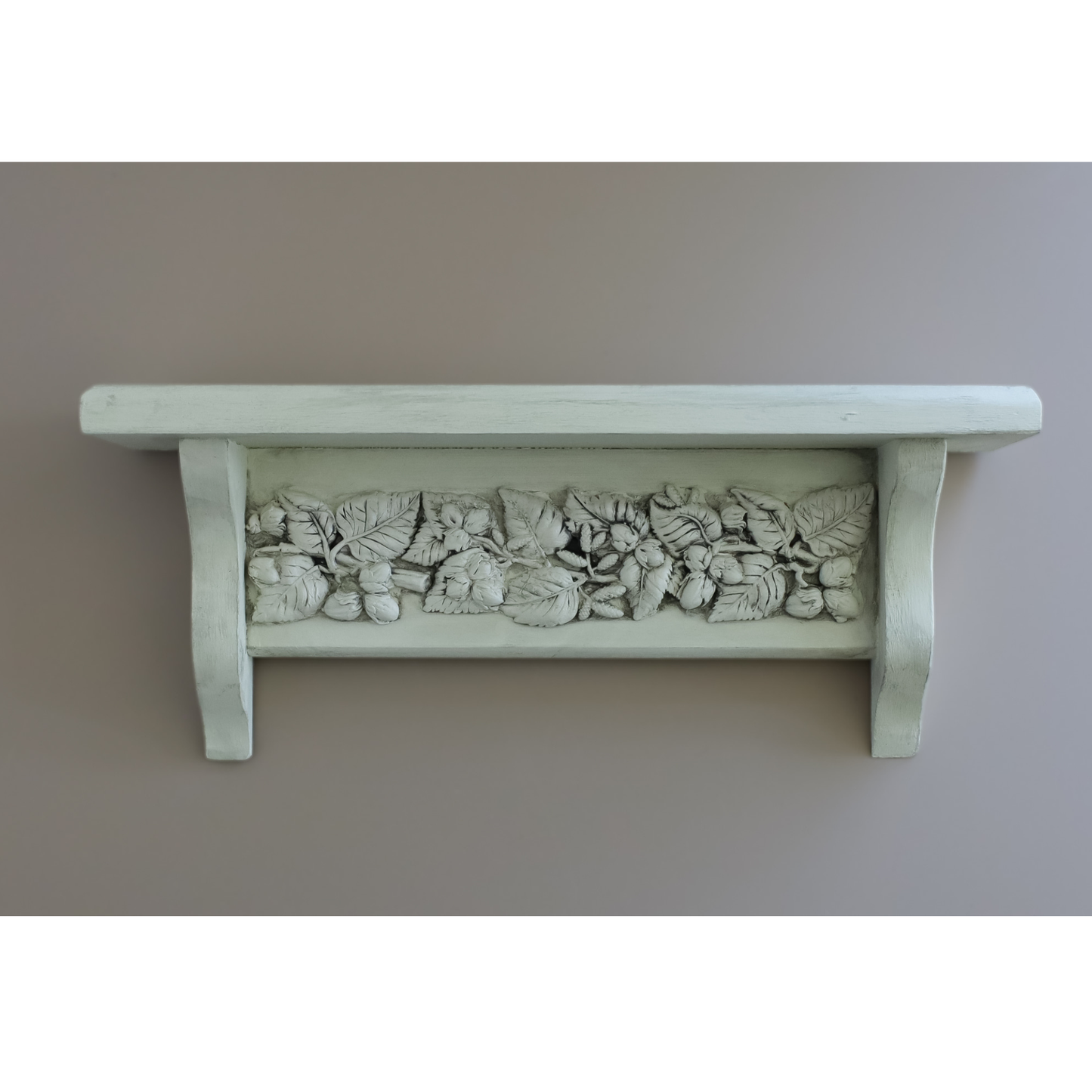 A white-painted wooden shelf with a detailed relief carving of grapes and leaves across the front, mounted against a plain taupe wall.
