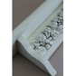 Close-up of a white decorative wall shelf with a raised leaf motif, shown against a plain taupe background.