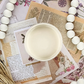 Image of open jar of light creamy beige paint on printed sepia ephemera with white beeds.