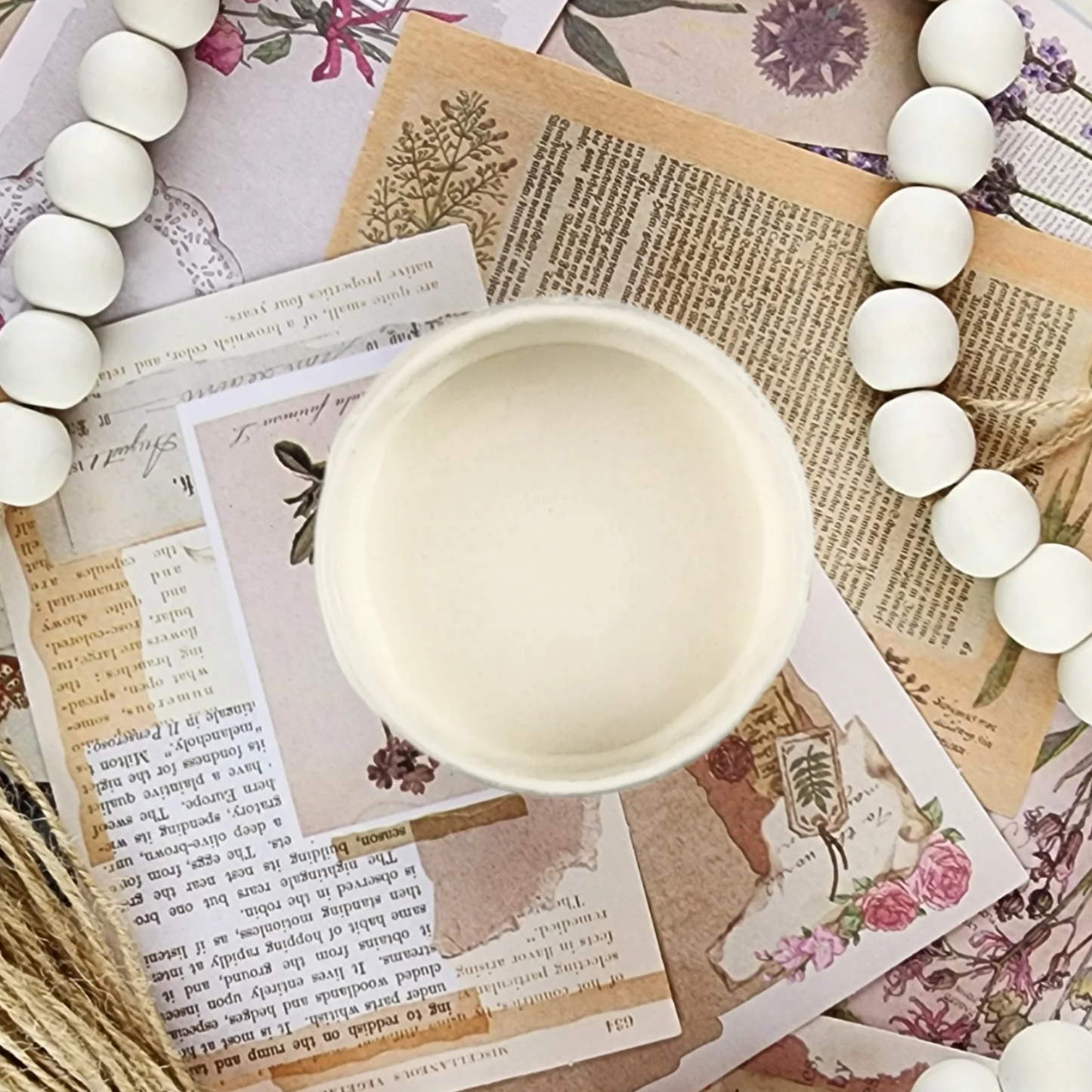 Image of open jar of light creamy beige paint on printed sepia ephemera with white beeds.
