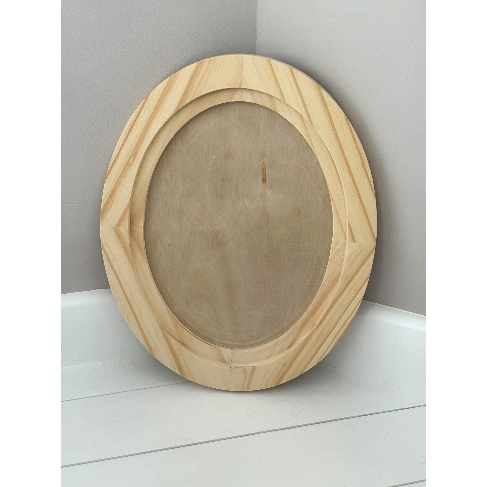 Large wooden oval frame on a white surface with a gray background
