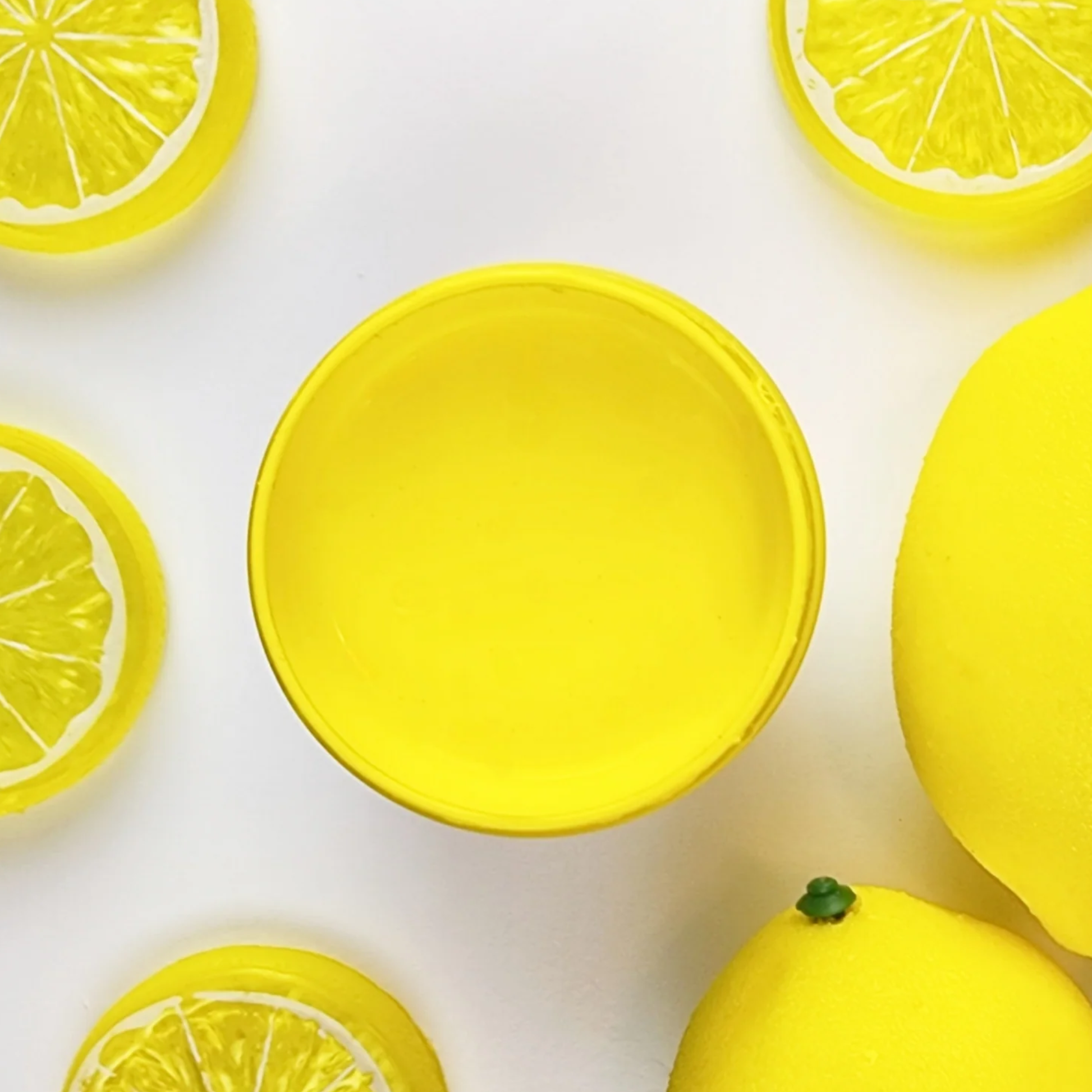 Image of open jar of bright yellow paint with lemon halves on a white background.