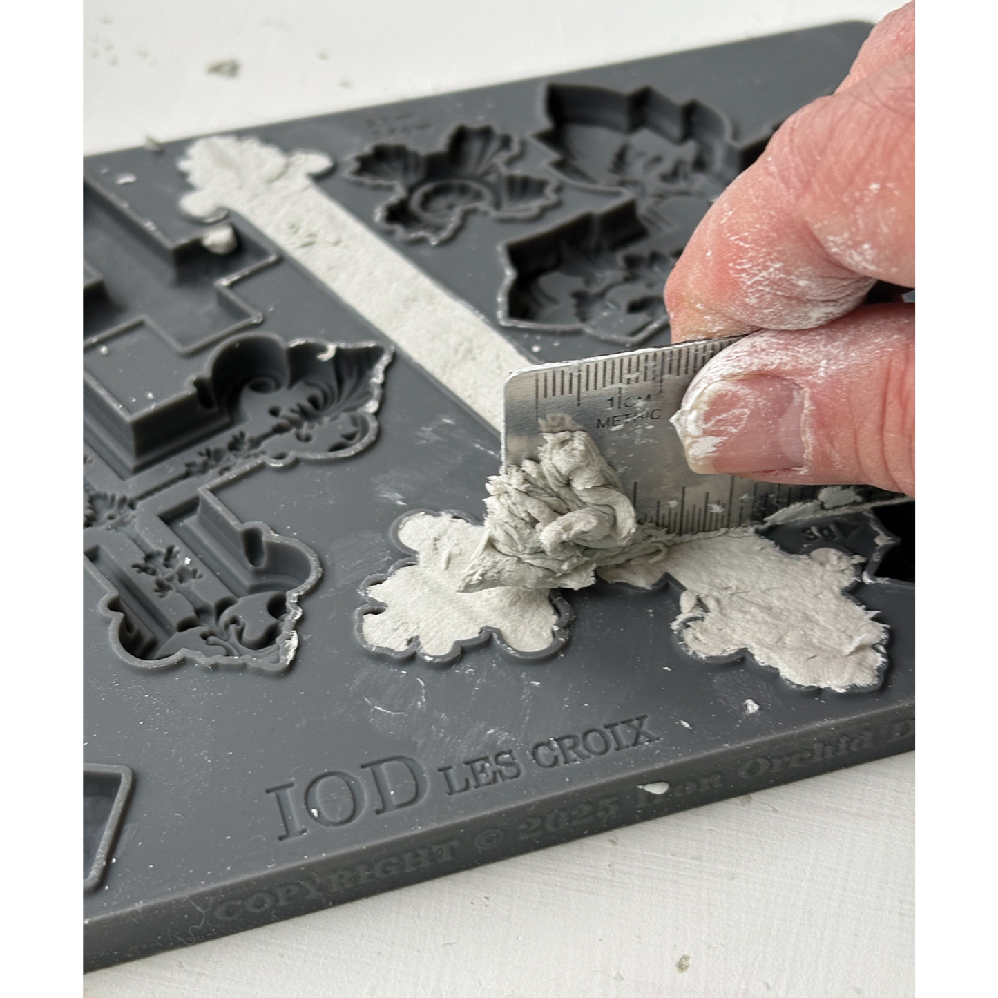 Person using a tool to shape gray material on a mold with 'IOD Les Croix' branding.