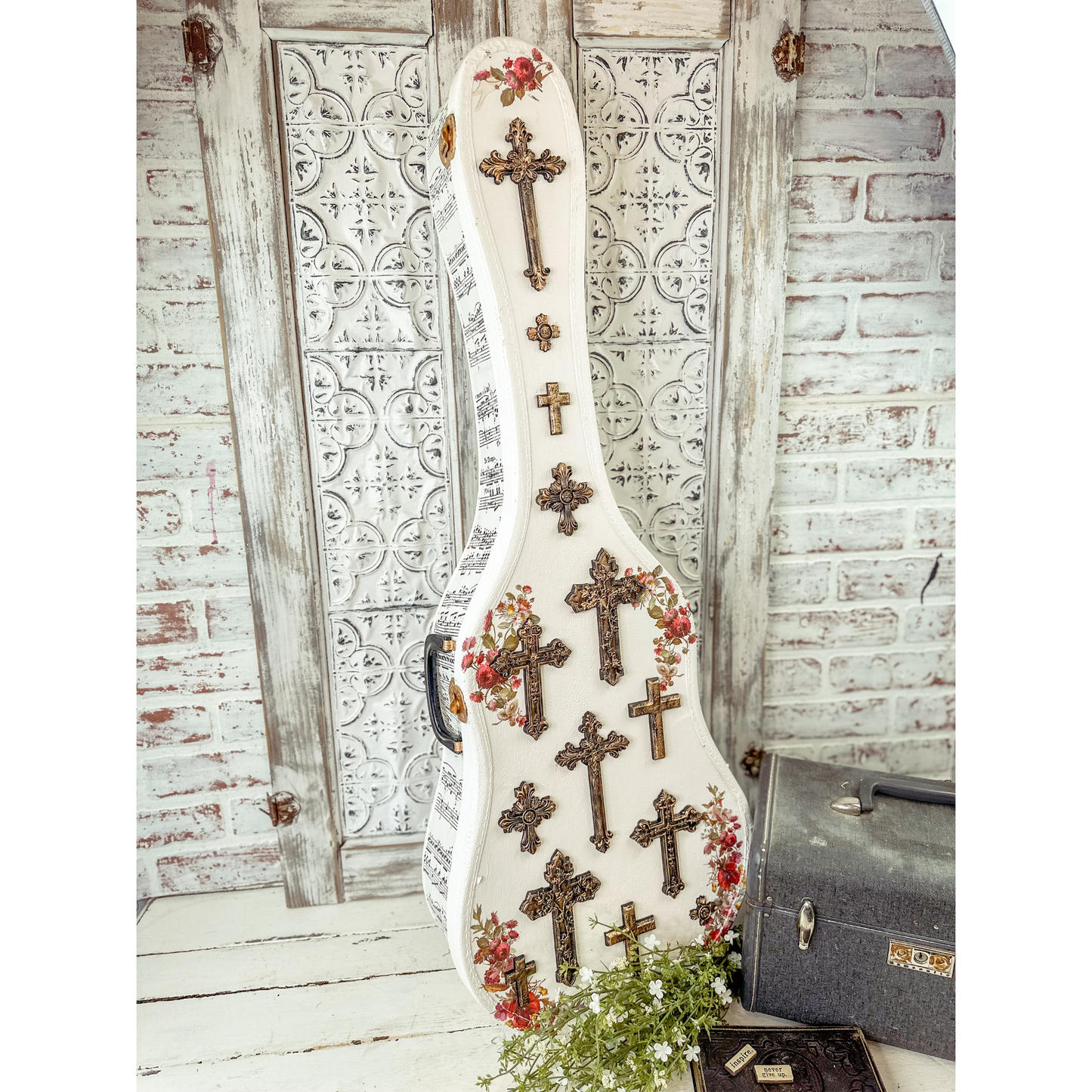 Decorative guitar case with cross patterns and floral designs against a rustic background.