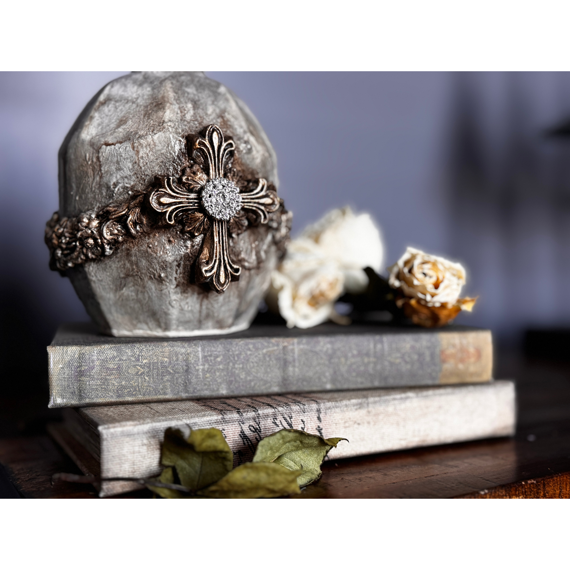 Decorative cross design on a stone block with books and flowers in the background