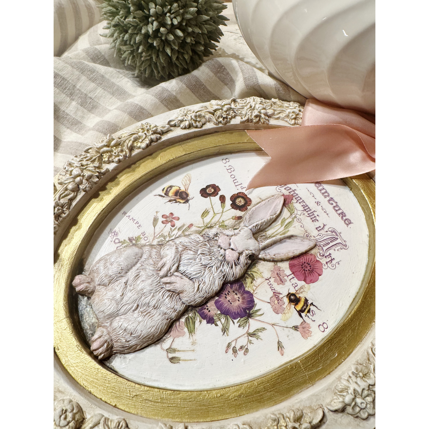 Decorative wall hanging with a rabbit, flowers, and a gold frame.