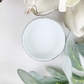 Image of open jar of greyish-white paint with leaves and flower petals on a white background.