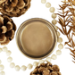Close-up of a pot of bronze metallic paint surrounded by pinecones and beads on a white background